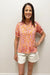 Woman wearing a patterned top and white shorts against a plain background