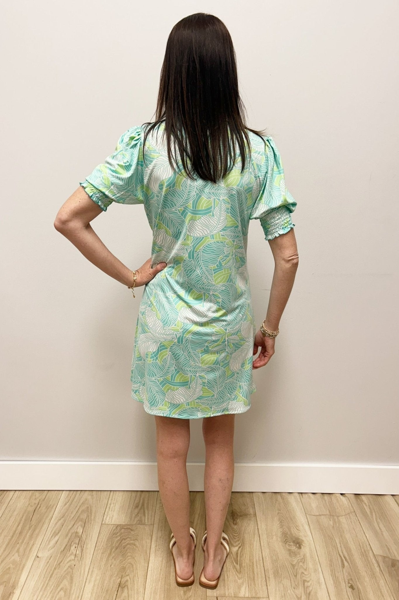 Woman wearing a light green floral dress against a plain wall.