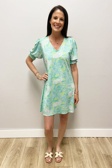 Woman wearing a light blue patterned dress standing against a white wall.