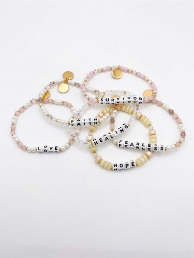 Six Little Words Project word bracelets in pearl, pink, peach, clear and cream beads on a white background
