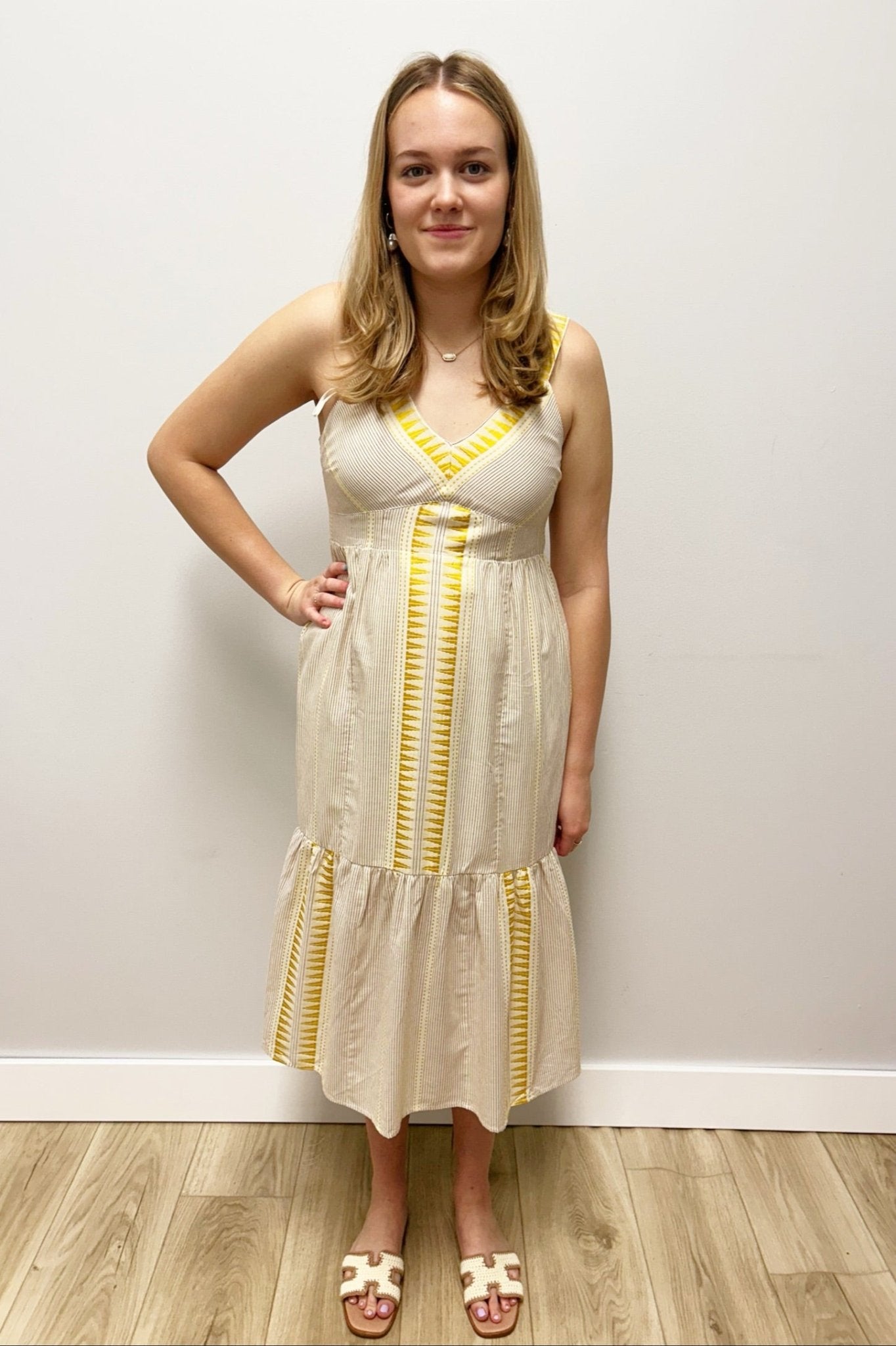 Woman wearing a beige dress with yellow accents against a plain wall.