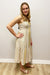 Woman wearing a beige dress with yellow trim against a plain wall.