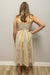 Woman wearing a beige and yellow dress against a plain wall.