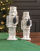 Two white ceramic nutcrackers beside a decorated Christmas tree