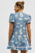 Woman wearing a blue dress with white pattern on a plain background - back view