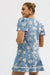 Woman wearing a blue dress with white patterns on a plain background - back side view