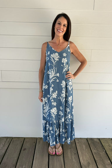 Woman wearing a blue floral dress standing on a wooden deck with a white wall background