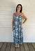 Woman wearing a blue floral dress standing on a wooden deck with a white wall background