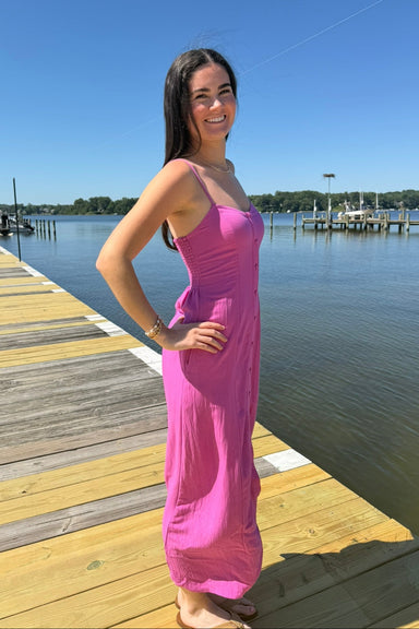 Woman in a pink dress standing on a dock by a body of water.