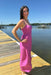 Woman in a pink dress standing on a dock by a body of water.