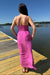 Woman in a pink dress standing on a wooden dock by a body of water.