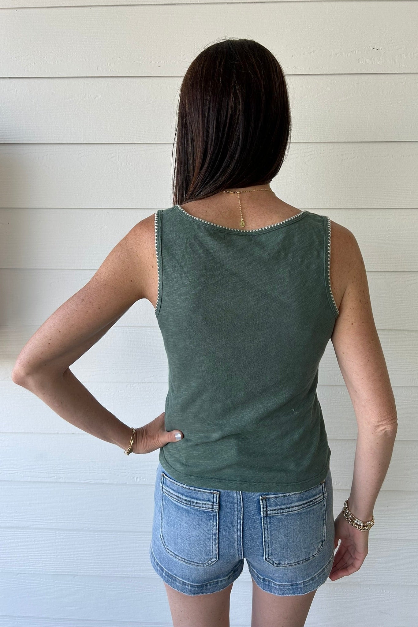 Woman wearing a green tank top and denim shorts against a white wooden panel background