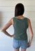 Woman wearing a green tank top and denim shorts against a white wooden panel background