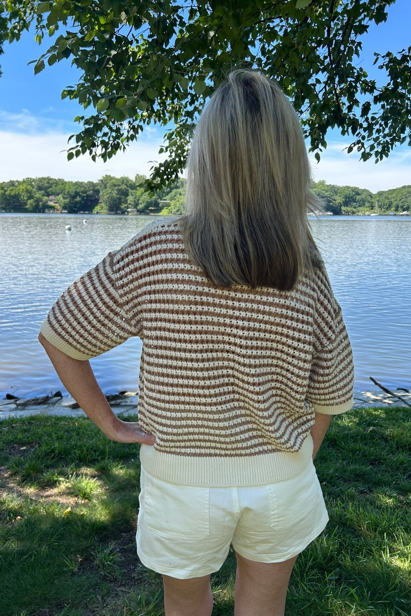 Person wearing a patterned sweater and white shorts standing by a lake