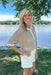 Woman standing by a lake wearing a patterned top and white shorts.