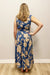 Woman wearing a blue floral dress standing against a plain wall.