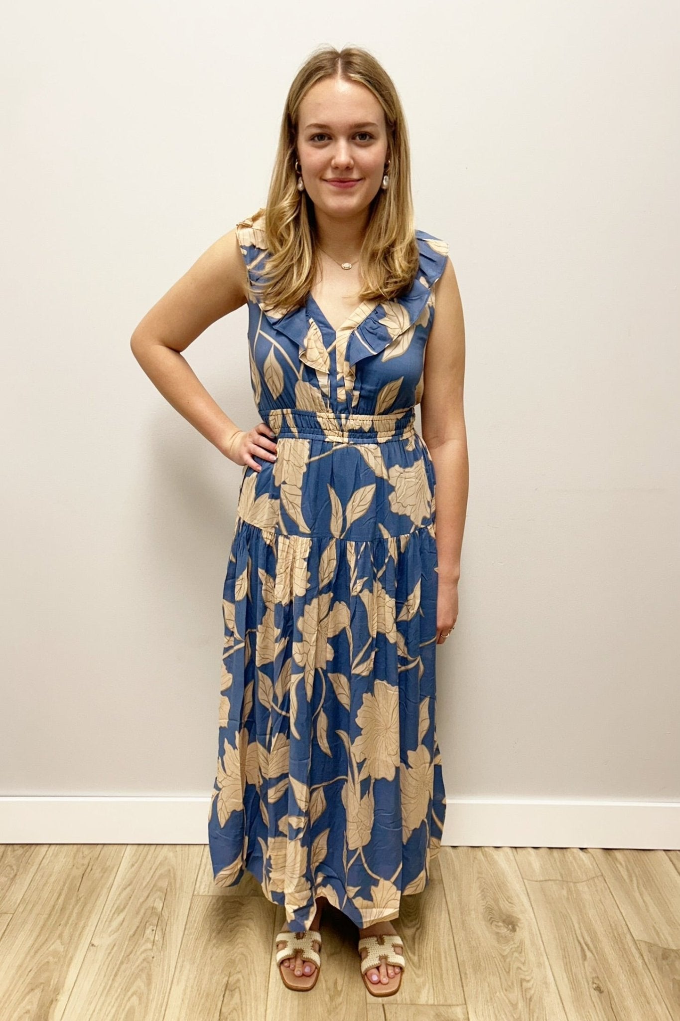 Woman wearing a blue floral dress standing against a plain wall.