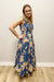 Woman wearing a blue floral dress standing against a plain wall.