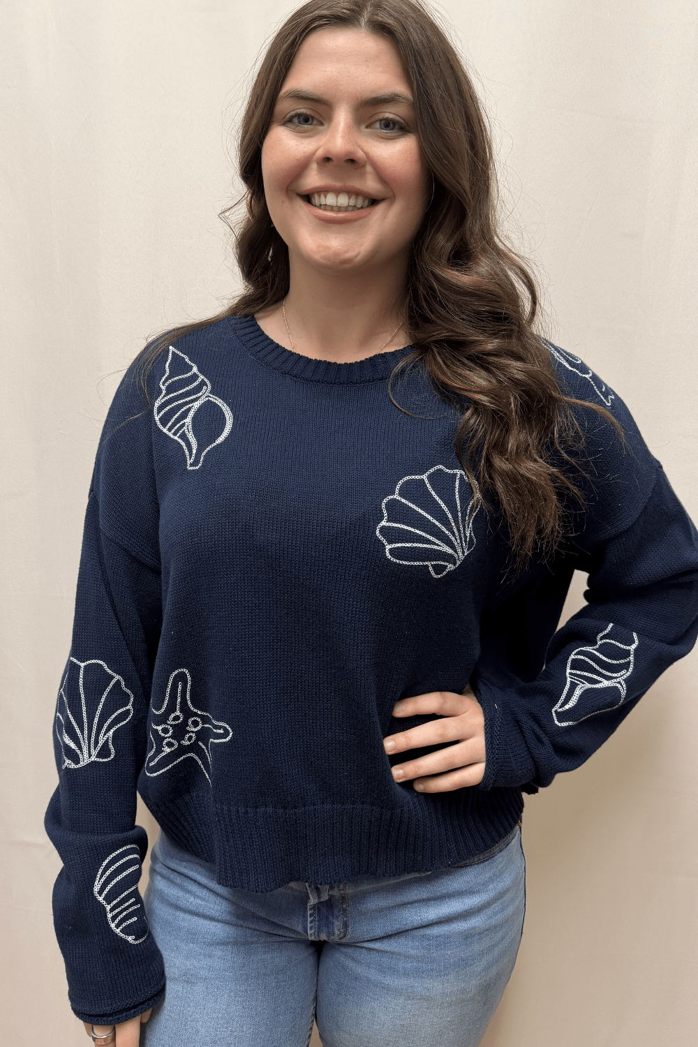 Ava wearing navy sweater with white embroidered seashells and starfish