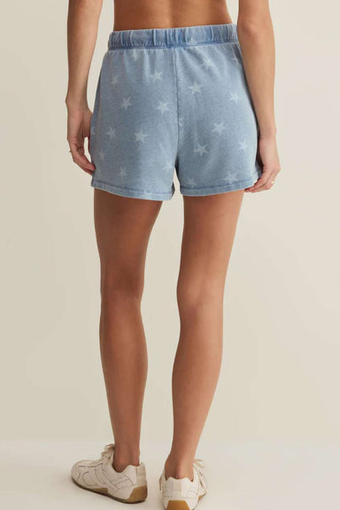 Person wearing light blue denim shorts with star pattern on a beige background