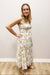 Woman wearing a floral dress standing against a plain wall.