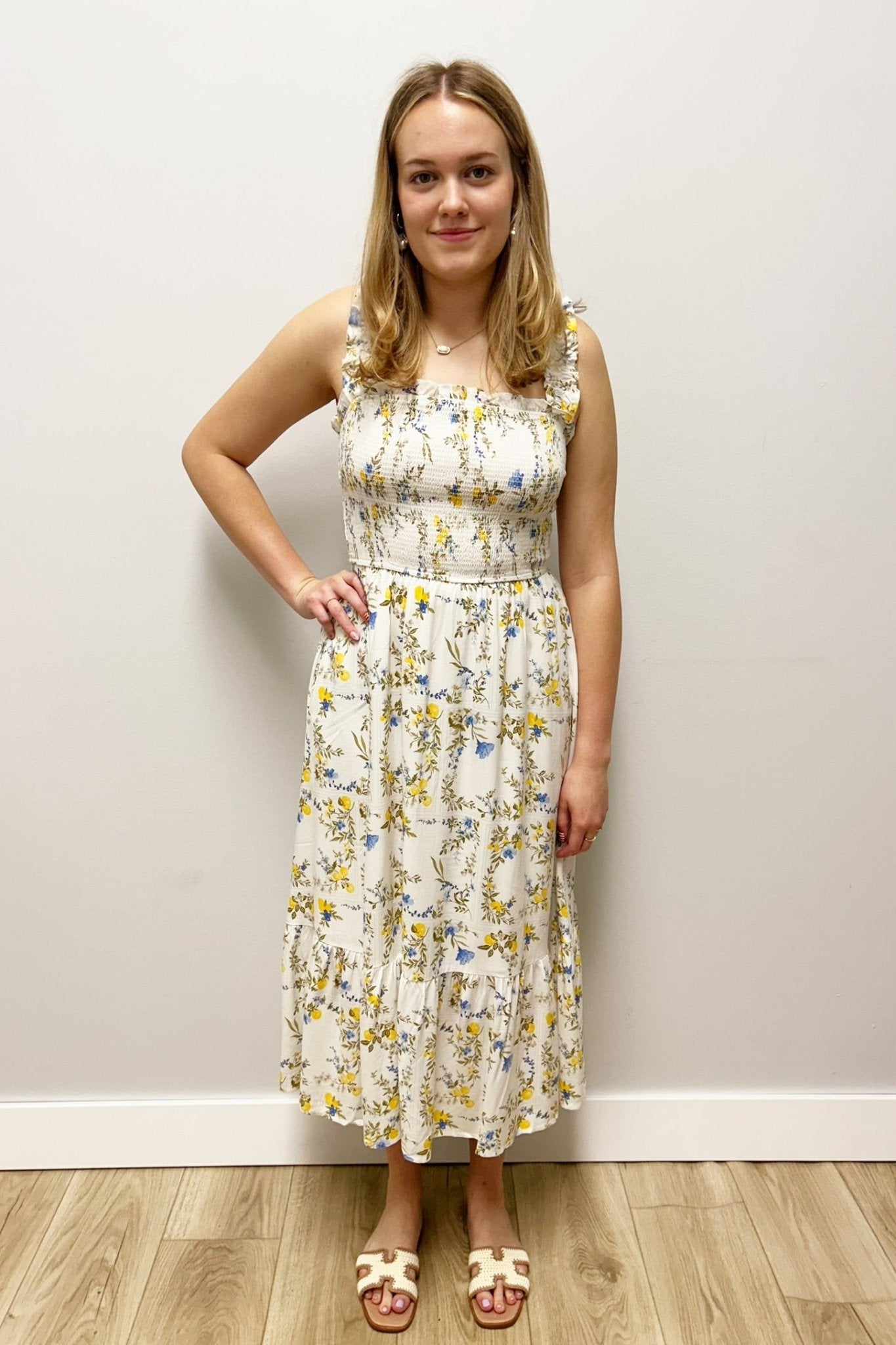 Woman wearing a floral dress standing against a plain wall.