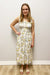 Woman wearing a floral dress standing against a plain wall.