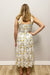Woman wearing a floral dress standing against a plain wall.
